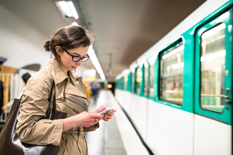 Girl using a mobile phone standing on a subway platform with a train arriving
